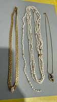 Overview of all three necklaces laid out: gold-tone collar, multi-strand pearls, pendant necklace