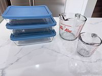 All three Pyrex containers with lids and two Fire-King pitchers on countertop