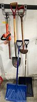 Group of two digging shovels, two snow shovels, hedge trimmer hanging on wall