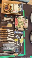Overview of cutlery, serving pieces, glass stirrer, honey dippers, skewers, spatula, and boxed souvenir spoon