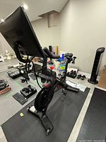 Front three-quarter view of Peloton Bike on mat with touchscreen, pedals, flywheel and accessories visible