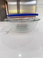 Side view of stacked clear glass bowls with blue and orange lids