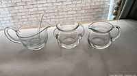 Three clear glass creamers side by side with ladle inserted in largest