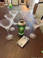 Six martini glasses, green glass cocktail shaker, box of cocktail picks on table