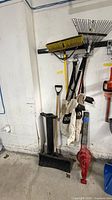 Full view of hanging tools: blower vac, rake, broom, shovel, bags, strap