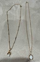 Both gold tone opal pendant necklaces laid flat
