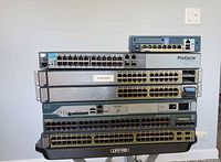 Front view of six stacked network devices showing port counts and manufacturer labels