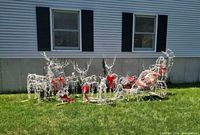 Multiple white wire-frame reindeer, wire-frame sleigh with inflatable Santa, red bows visible on grass
