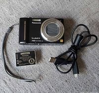 Front view of camera with lens closed, battery and cable visible