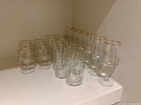 Group of glassware showing footed sherbets and cylindrical tumblers with gold rims