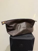 Front view of brown Paco Rabanne Parfums cosmetic bag on stand