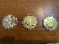 Fronts of three gold-plated commemorative coins: Beatles portraits, Oscar statue with filmstrip, Aztec calendar