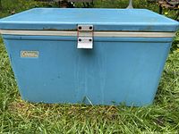 Front view of blue Coleman cooler showing logo badge, broken latch with rubber band