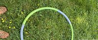 Full view of green/grey segmented weighted hula hoop on grass