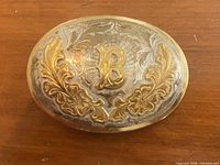 Front of oval belt buckle showing gold-tone letter B and scrollwork