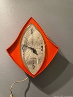 Front view showing entire orange diamond-shaped clock with cord