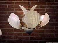 Chandelier lit to show frosted glass shell shades and brass arms