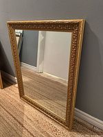 Full view of rectangular gold-gilt framed mirror leaning against wall