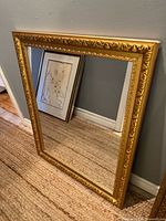 Full view of gold gilt framed mirror leaning against wall