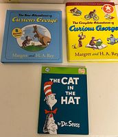 Three hardcover children’s books laid out: The New Adventures of Curious George, The Complete Adventures of Curious George, The Cat in the Hat