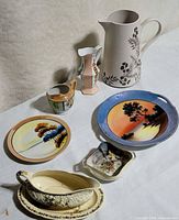 Assorted ceramic pieces laid on table including pitcher, plates, gravy boat, vase and dishes