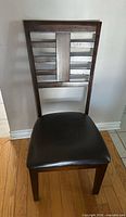 Front view of dark brown ladder-back dining chair with black faux leather seat
