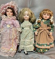 Front view of three porcelain dolls displaying outfits and sizes