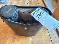 Binoculars stored in leather case with cap visible and lot tag