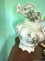 Side view of porcelain pitcher showing scalloped rim and floral transfer