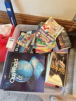 Plastic bin holding assorted paperbacks, Archie digests and hardcover atlas
