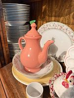 Coral teapot, stacked plates, yellow plate, floral bowl, rooster dish visible