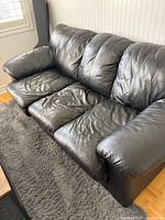 Front view of black leather three-seat sofa showing seat and arm condition