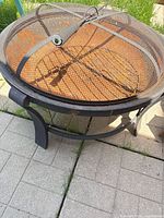 Overall view of fire pit with mesh lid and poker showing rusted interior