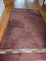 Full view of brown wool rug on hardwood floor showing both decorative stripe ends