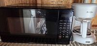 Overall view of black microwave and white Mr. Coffee coffee maker on shelving