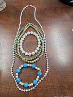 All five pieces laid out: three necklaces (ivory faux pearl, champagne faux pearl, green glass beads) and two bracelets (ivory pearl, turquoise & pearl)