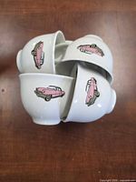 Four cups stacked showing pink car decals on white ceramic