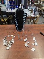 Overview of all three necklaces and accompanying earrings displayed on table and bust