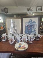 Group shot of both framed prints, 12 mugs, 2 plates displayed on table