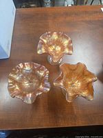Top view of three ruffled marigold carnival glass compotes showing iridescent finish and embossed floral pattern