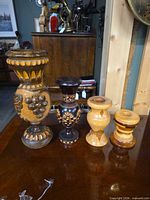 Front view of four wooden candle holders showing carving, paint, height differences