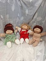 Three Cabbage Patch Kids dolls posed together showing clothing and condition