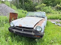 Front view of rusted MG convertible showing grille, headlights, missing bumper, windshield