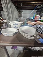 Group of CorningWare dishes, clear bowls and pottery dish on table