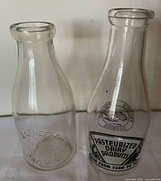 Front view of both glass milk bottles showing embossing and pyro-glaze