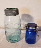 Front view of aqua Crown Imperial mason jar with zinc lid alongside cobalt blue wire-bale canister