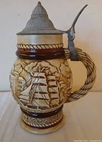 Right side profile showing ship scene, braided handle, pewter lid