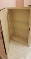 Cabinet open showing cream enamel interior and two glass shelves