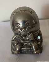 Front view of silver-plated Humpty Dumpty coin bank showing facial features and bow tie