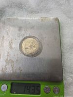 Coin in plastic capsule on digital scale showing 14.35 g